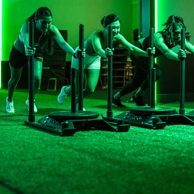 gym members push weighted sleds during a signature group fitness class at emerald city athletics gym near me